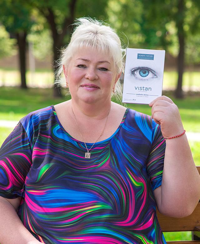 Natural Pharmaceuticals Vistan Moteris lauke sėdi ant suoliuko ir laiko akių sveikatai skirtą maisto papildą „Vistan“.