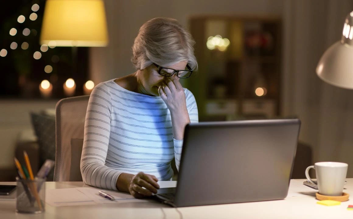 Natural Pharmaceuticals Vistan Vidutinio amžiaus moteris darbe prie kompiuterio vakare, jaučianti akių nuovargį ir stresą.